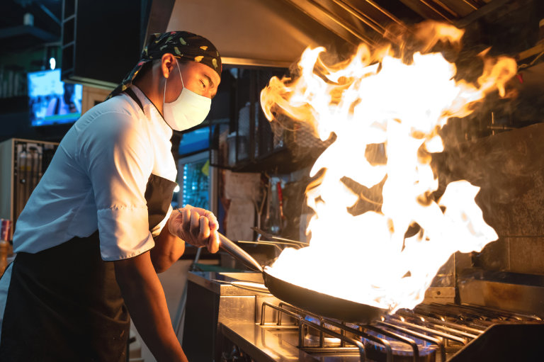 Koch arbeitet in einem Restaurant und flambiert das Essen.